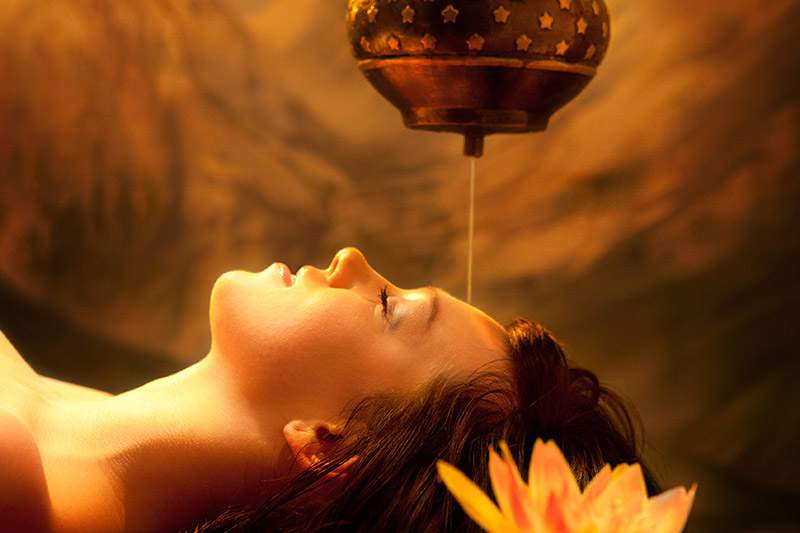 An image of Ayurvedic oil being poured on a woman's forehead